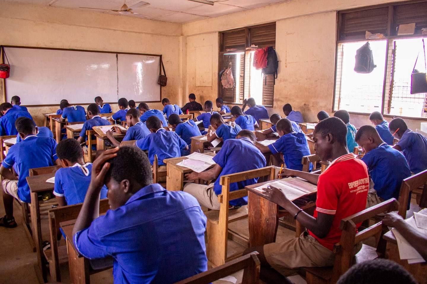 Students in school uniform writing an exam in a classroom, heads down over their papers